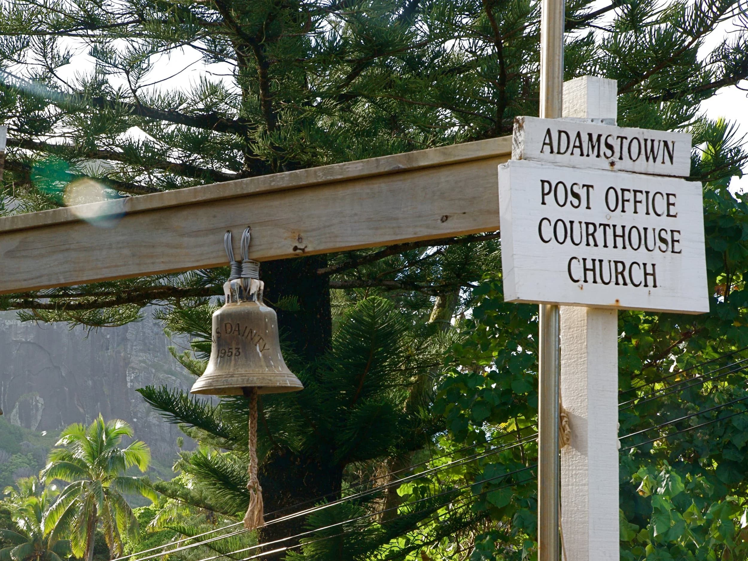 The Adamstown sign pointing to the post office, courthouse and church, beside an old bell