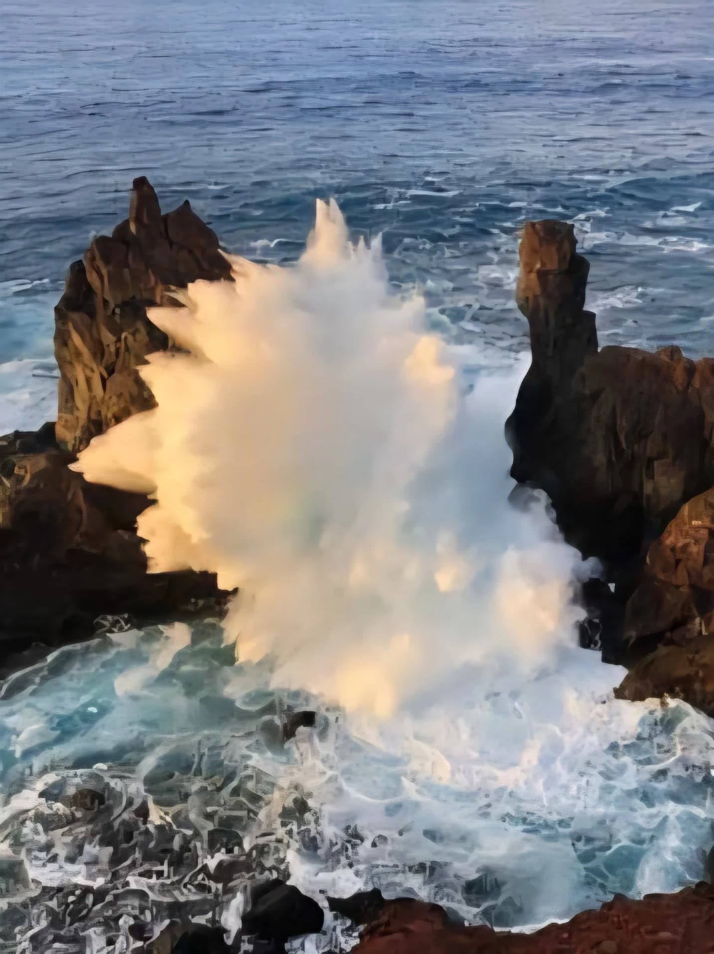 A wave bursting white between dark volcanic rocks