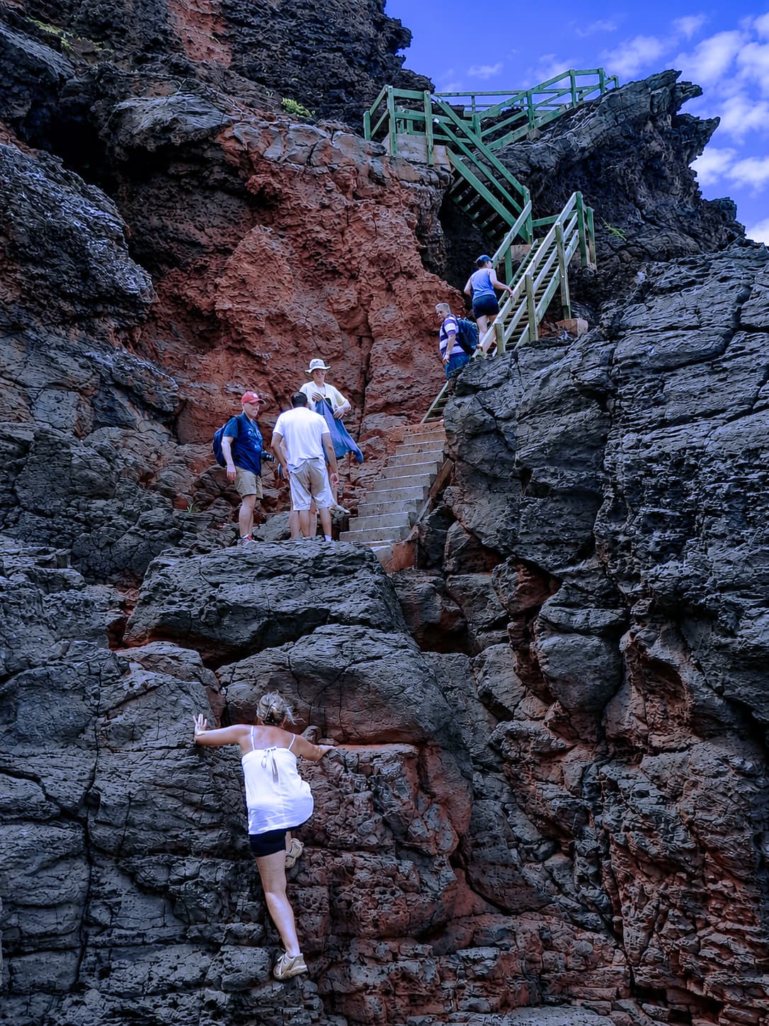 Walkers climbing a steep path and steps through dark volcanic rock