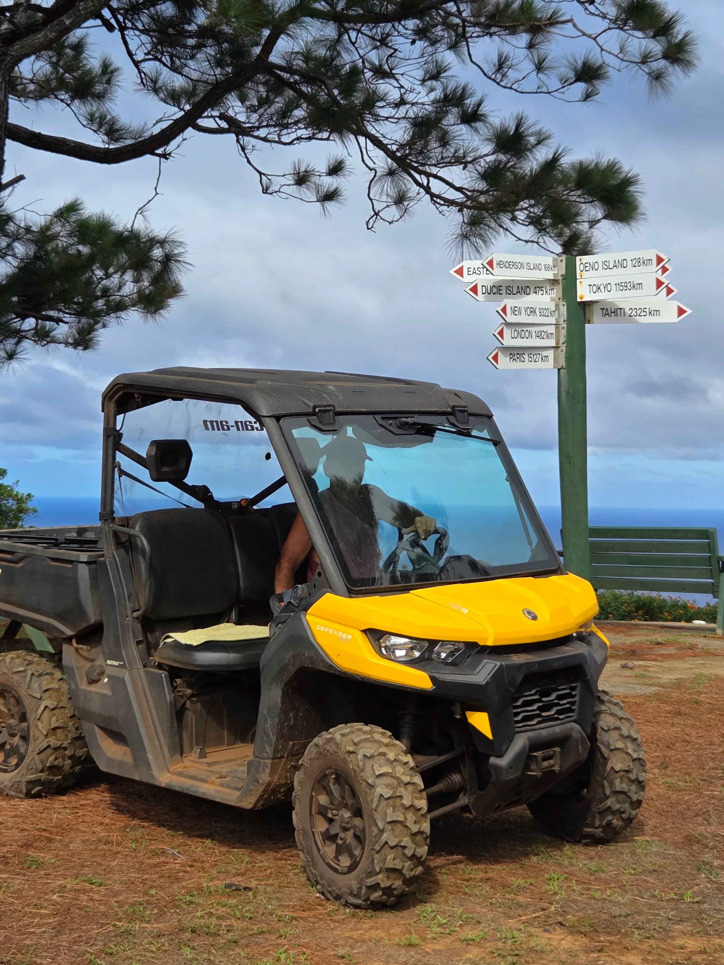 A yellow all-terrain vehicle beside a signpost under tall trees