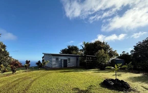 A small house on a mown lawn among trees, under a wide blue sky